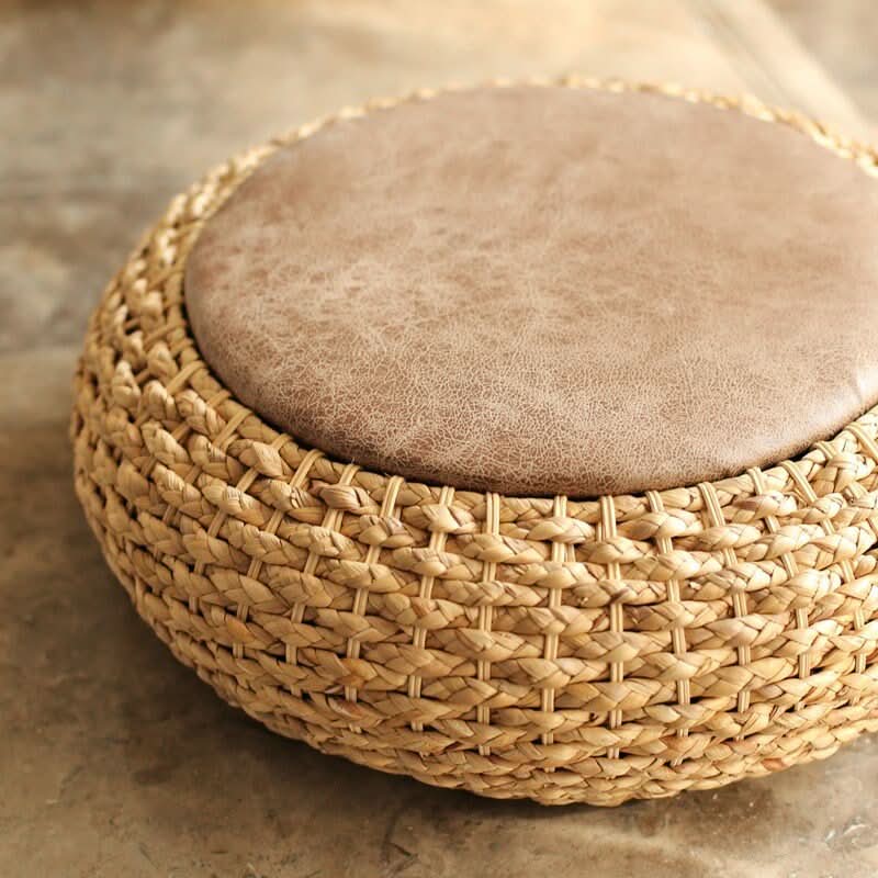Cattail Woven Round Futon with distressed brown leather top on textured floor.
